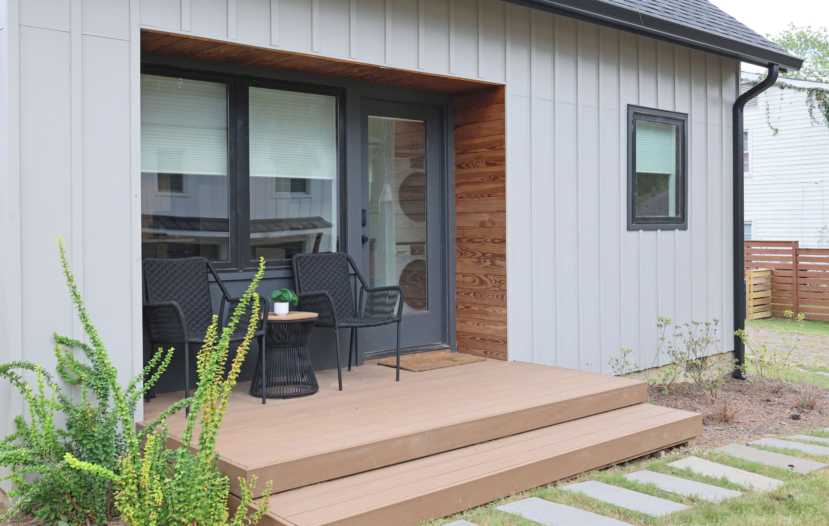 A modern outdoor seating area with a wooden deck, black wicker chairs, and a small table.