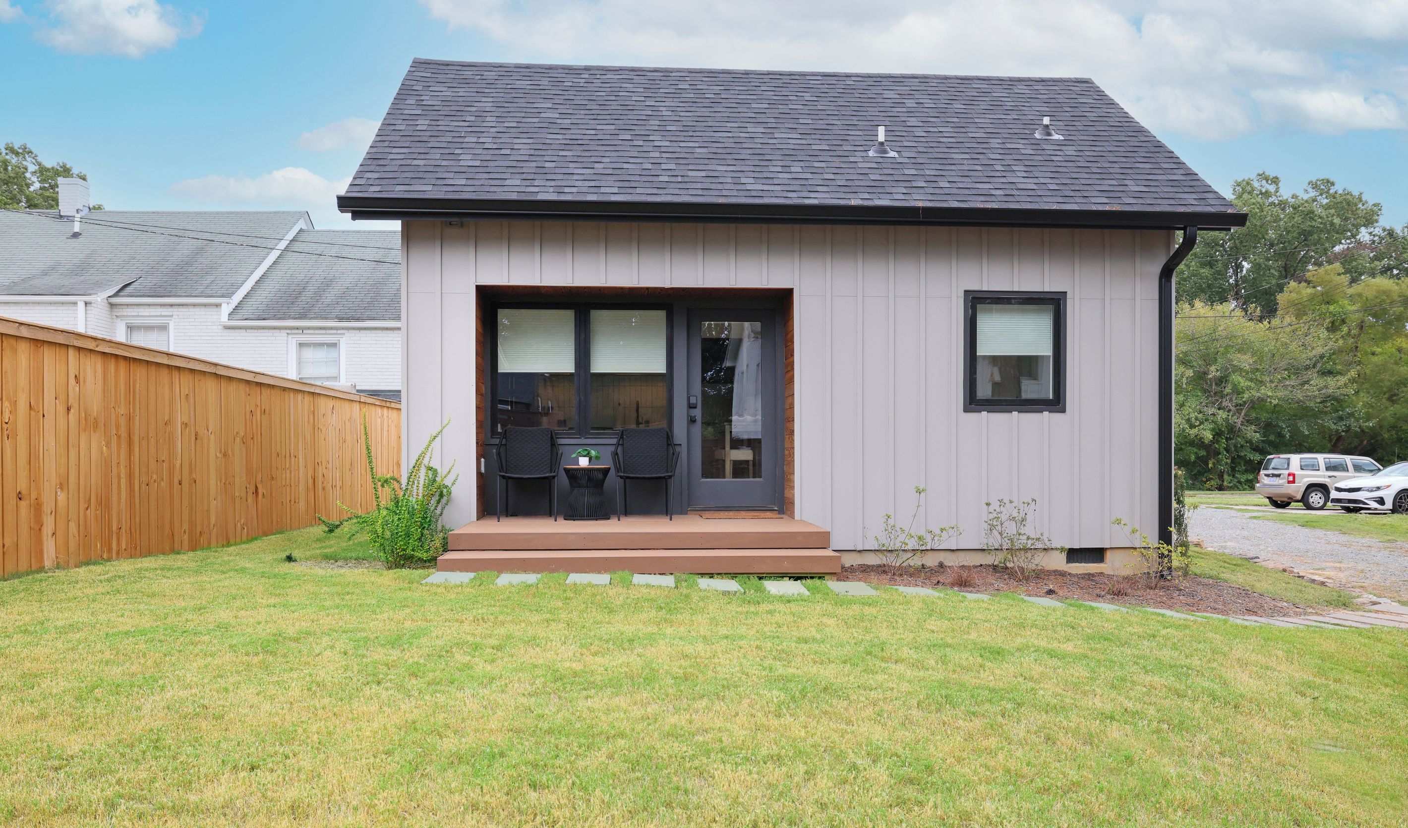 A modern single-story house with a dark roof, a front door, and a small patio area with a table and chairs.