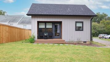 A modern single-story house with a dark roof, a front door, and a small patio area with a table and chairs.