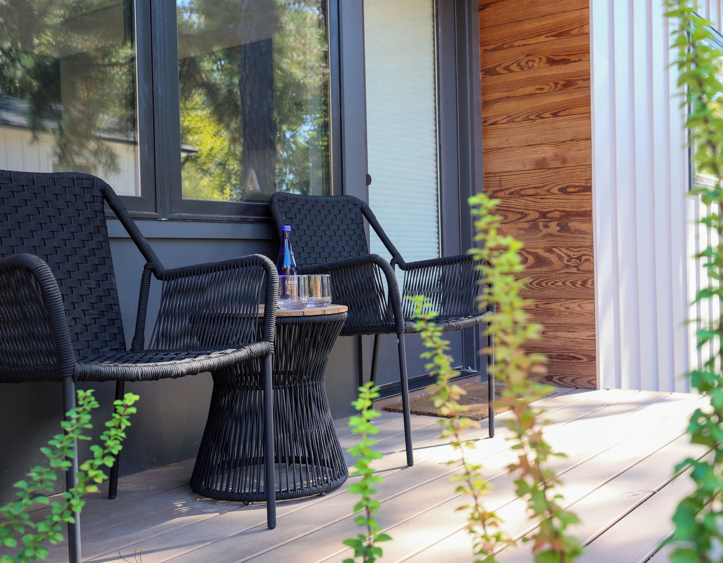 A modern outdoor seating area with wicker chairs and a table, a wooden wall, and a window.