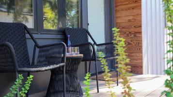 A modern outdoor seating area with wicker chairs and a table, a wooden wall, and a window.