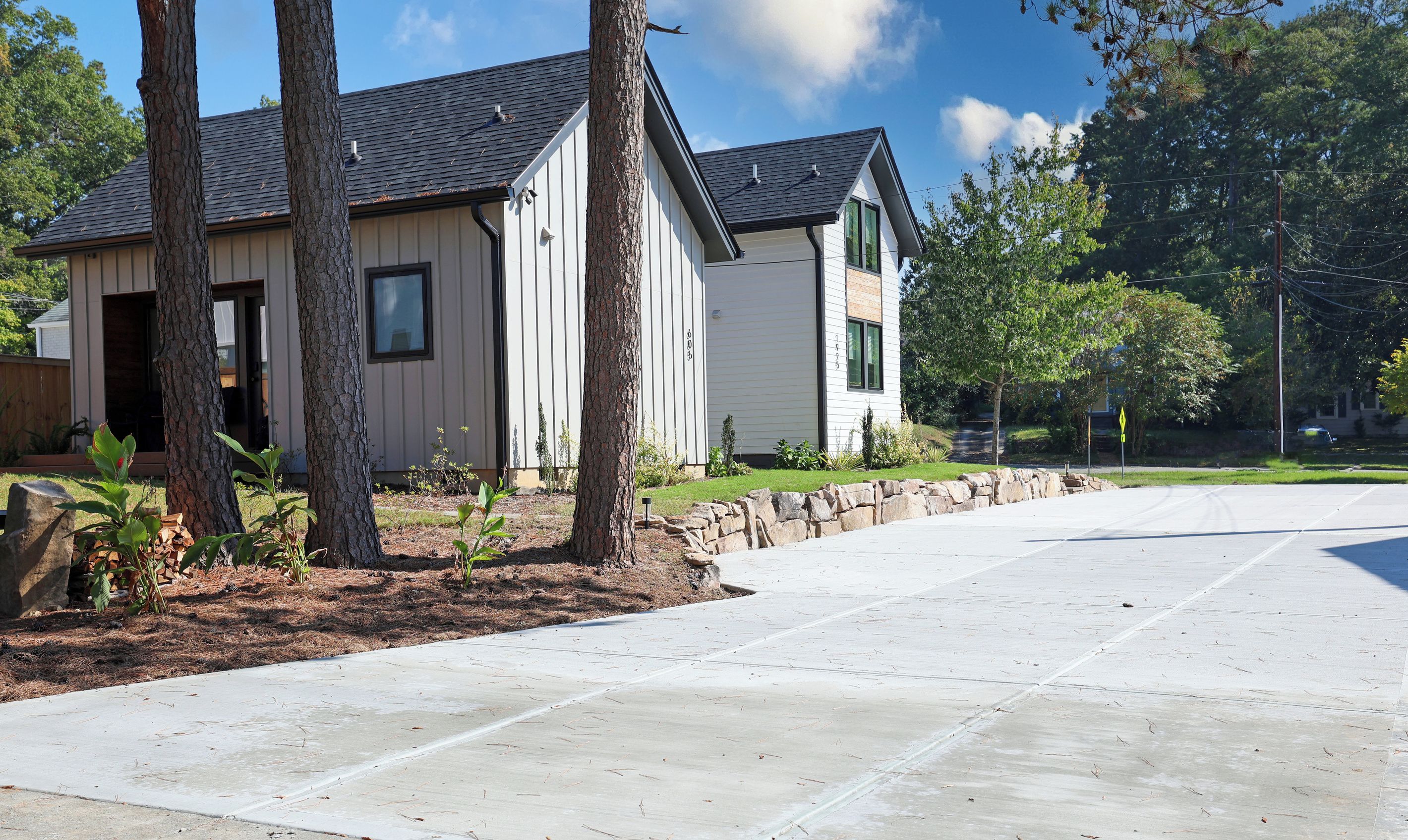 A residential property with a driveway, trees, and a stone wall.