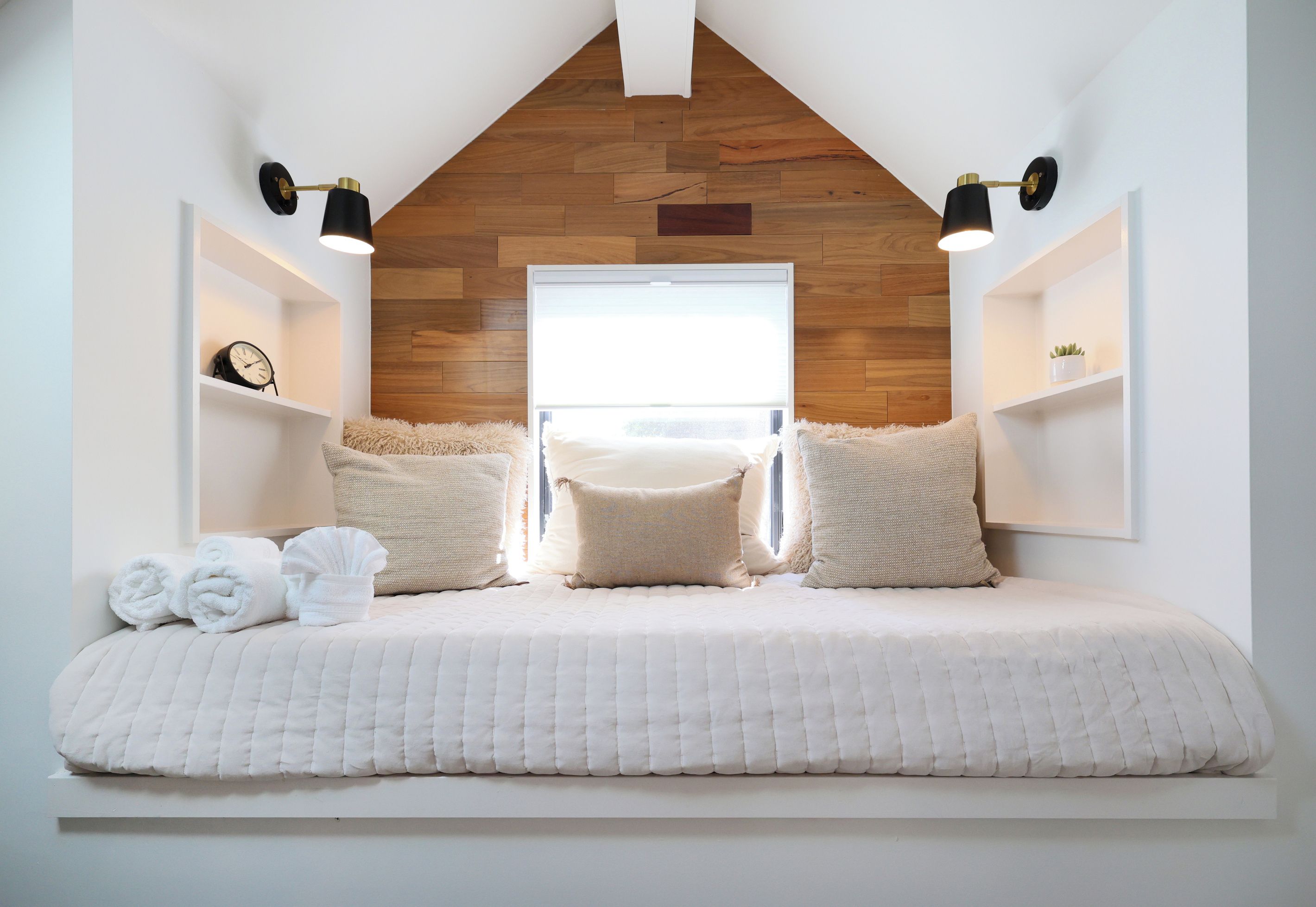 A bedroom with a sloped ceiling, a bed with white bedding, two bedside tables, and a wooden wall panel.