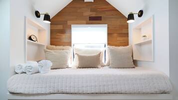 A bedroom with a sloped ceiling, a bed with white bedding, two bedside tables, and a wooden wall panel.