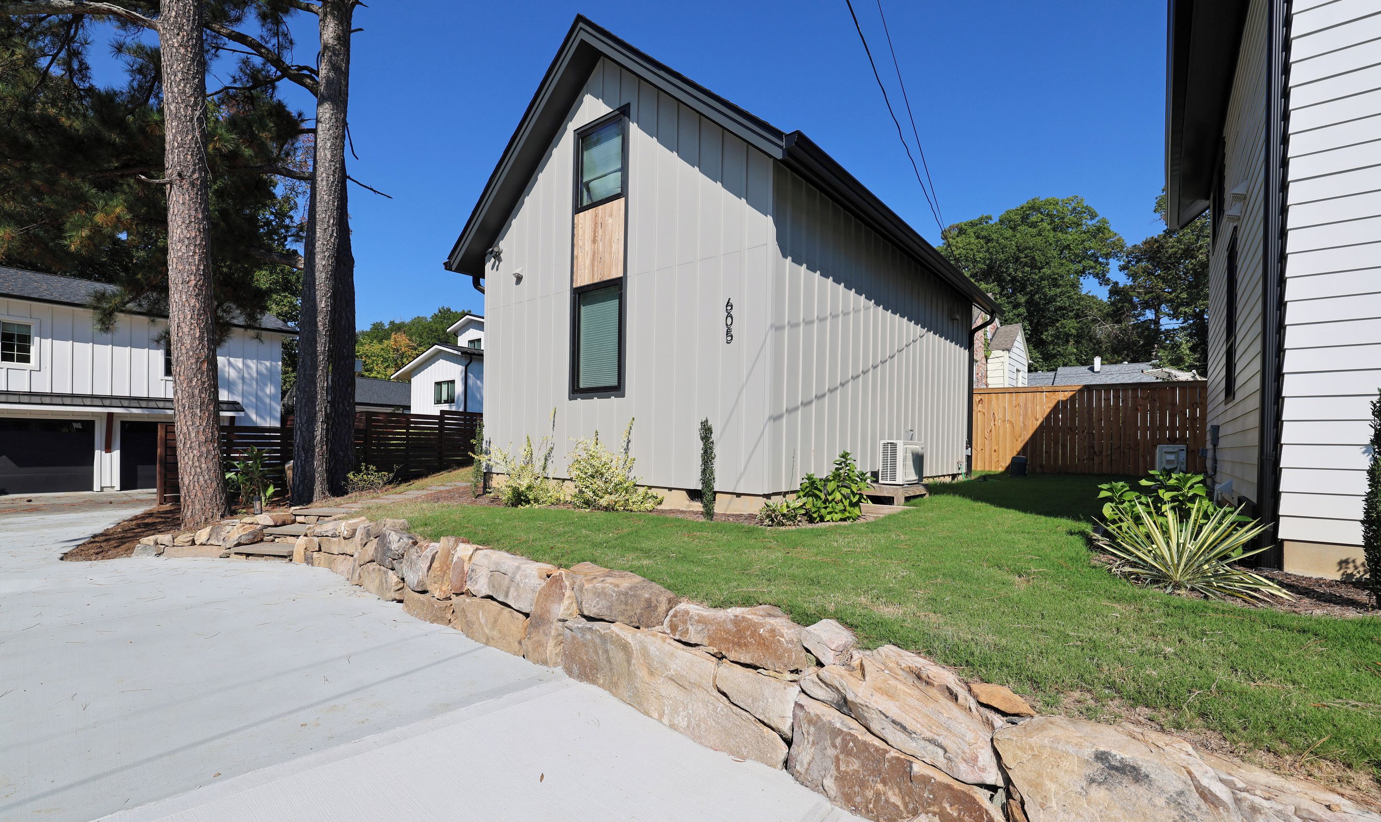 A modern two-story house with a stone retaining wall, a well-maintained lawn, and a clear blue sky.