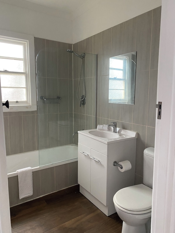 A bathroom with a shower, toilet, sink, and a window.