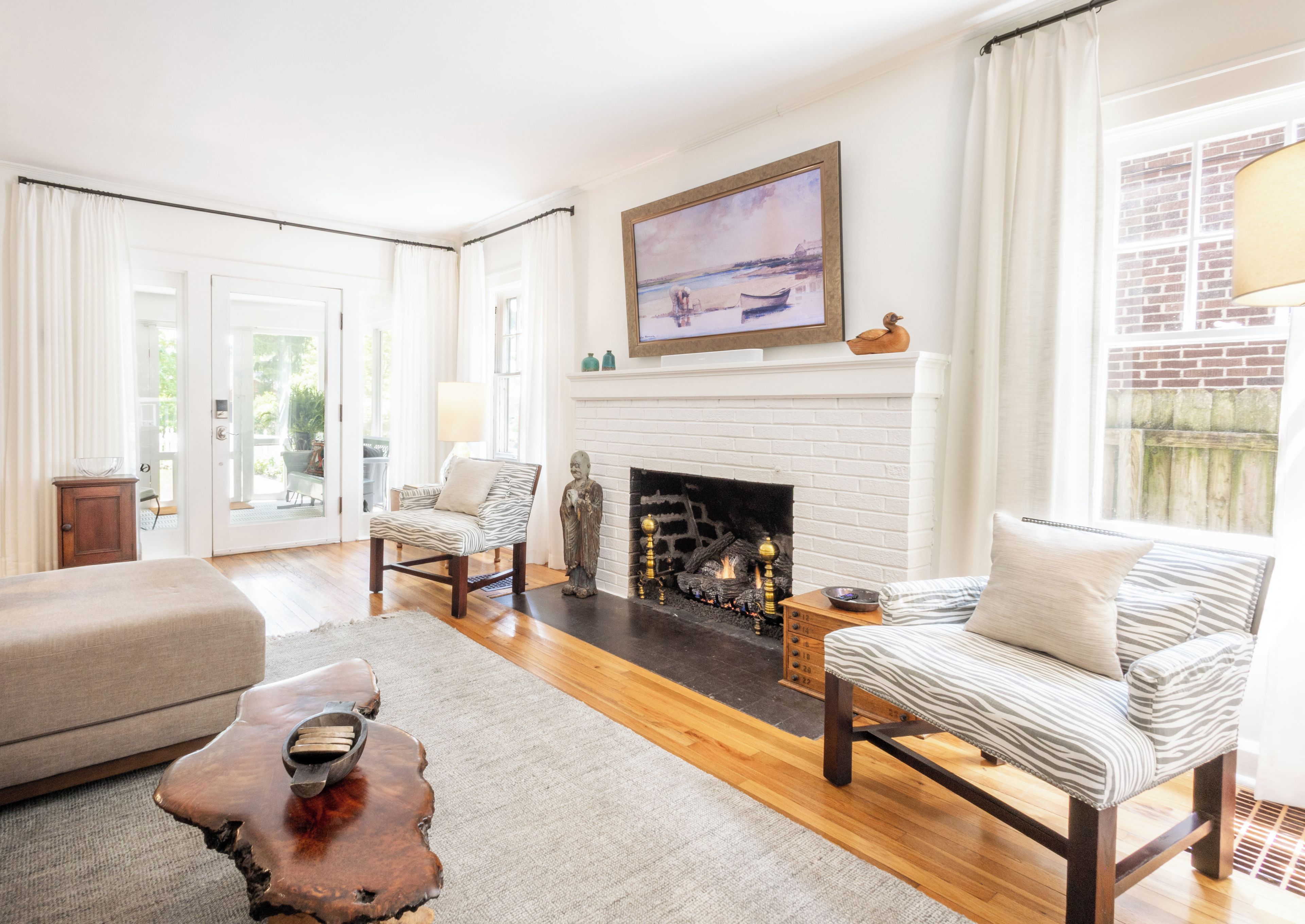 A living room with a fireplace, a zebra-striped sofa, a wooden coffee table, and a painting above the fireplace.