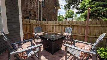 A patio with a table and four chairs, a wooden fence, and a house in the background.