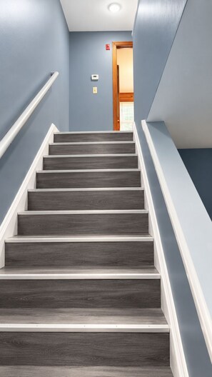 Un escalier avec des marches en bois foncé et des rampes blanches, menant à une porte située en haut.