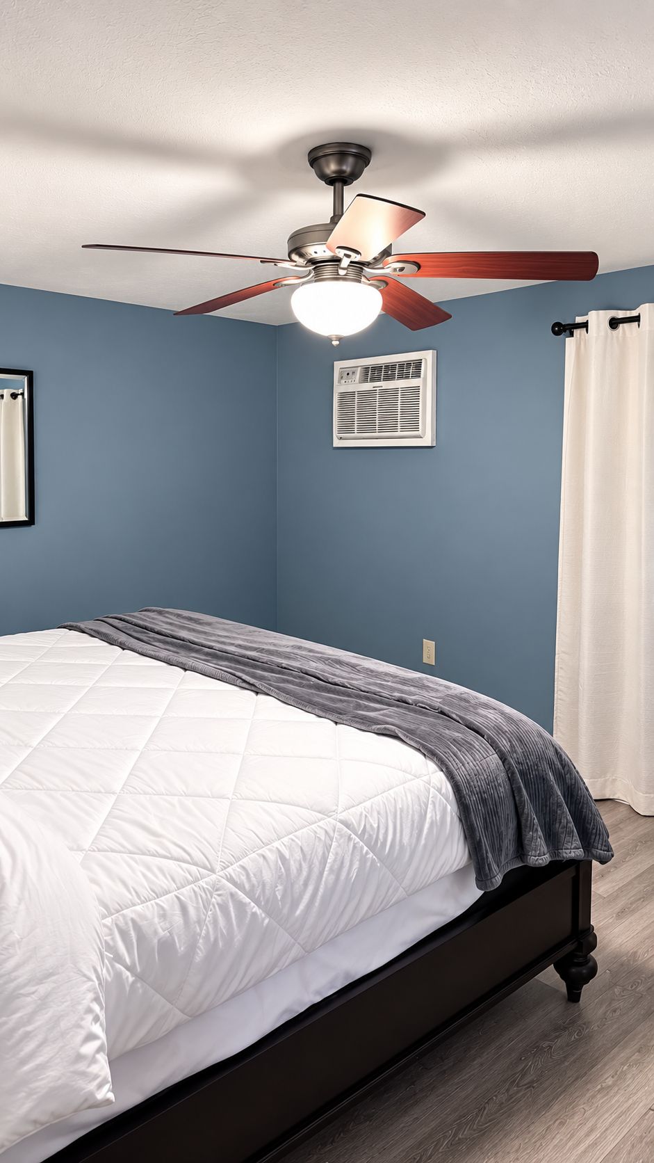 Een slaapkamer met een bed, een plafondventilator, een airconditioning en een raam met gordijnen.