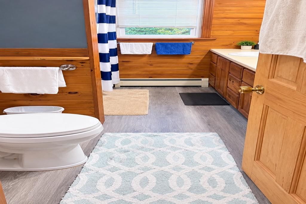 Un baño con inodoro, un tapete, armarios de madera, un ventanal con vistas y un perchero para toallas.