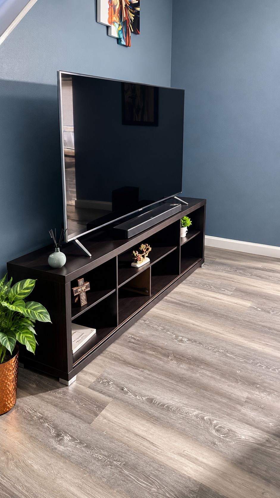 A modern living room with a dark wooden entertainment unit, a flat-screen TV, and a potted plant.