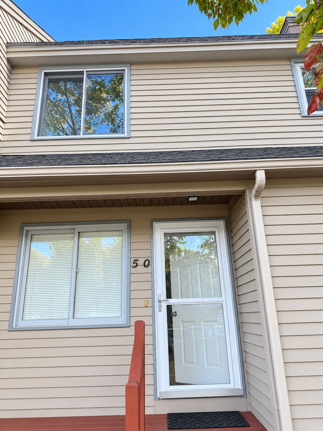 A two-story building with a beige siding exterior, a front door with a glass panel, and two windows with blinds.