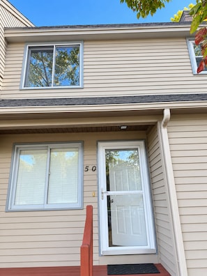 A two-story building with a beige siding exterior, a front door with a glass panel, and two windows with blinds. - Cozy & Stylish 2-bedroom 1.5 bath townhouse in central MAss Home Getaway. (Leominster)