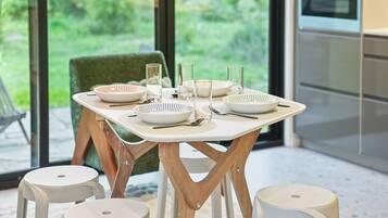 A dining table set with plates, glasses, and cutlery, positioned near a window with a view of greenery.