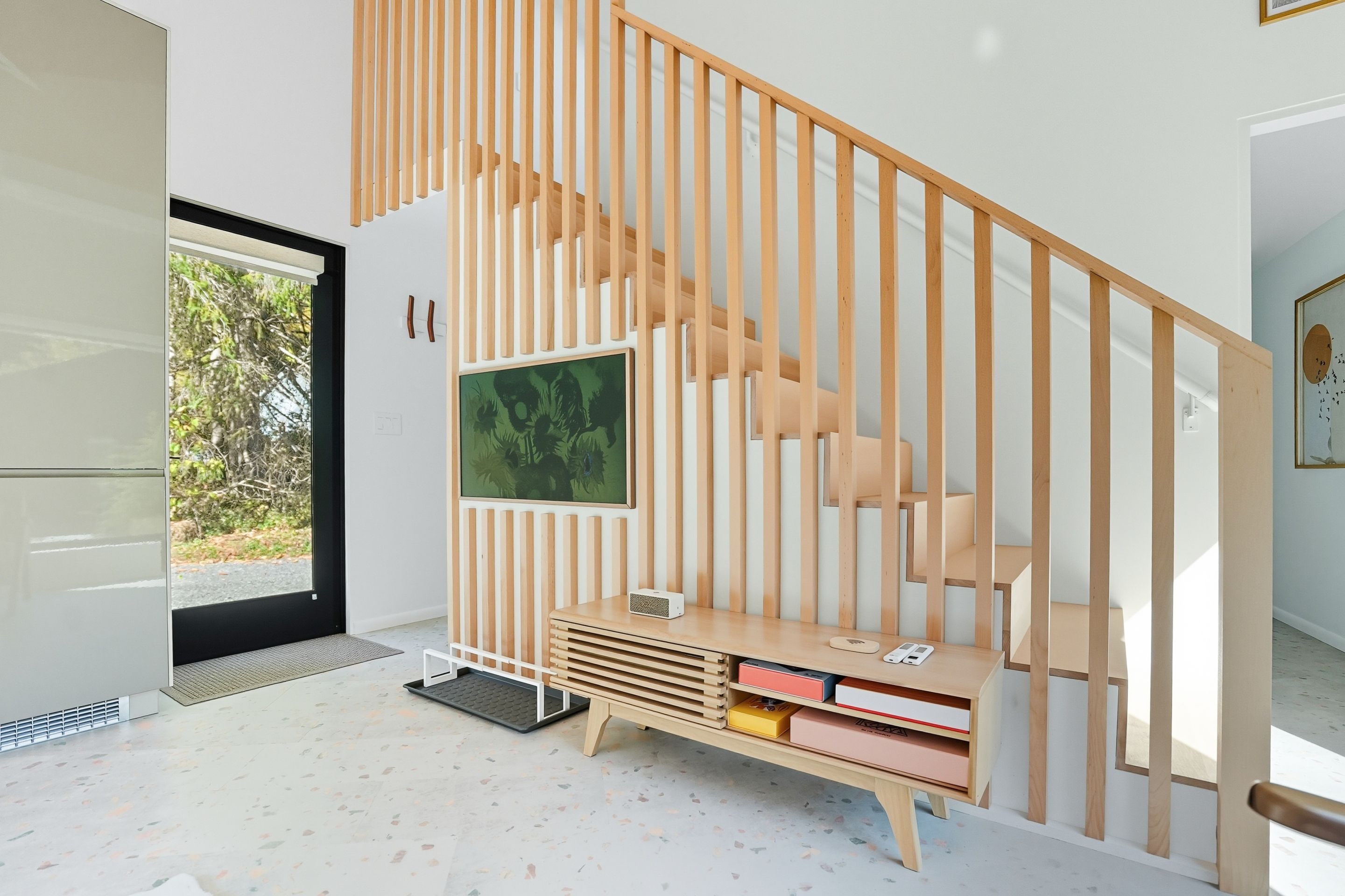 Un interior moderno con una escalera de madera, un televisor de pantalla plana montado en la pared y una estantería empotrada llena de libros.