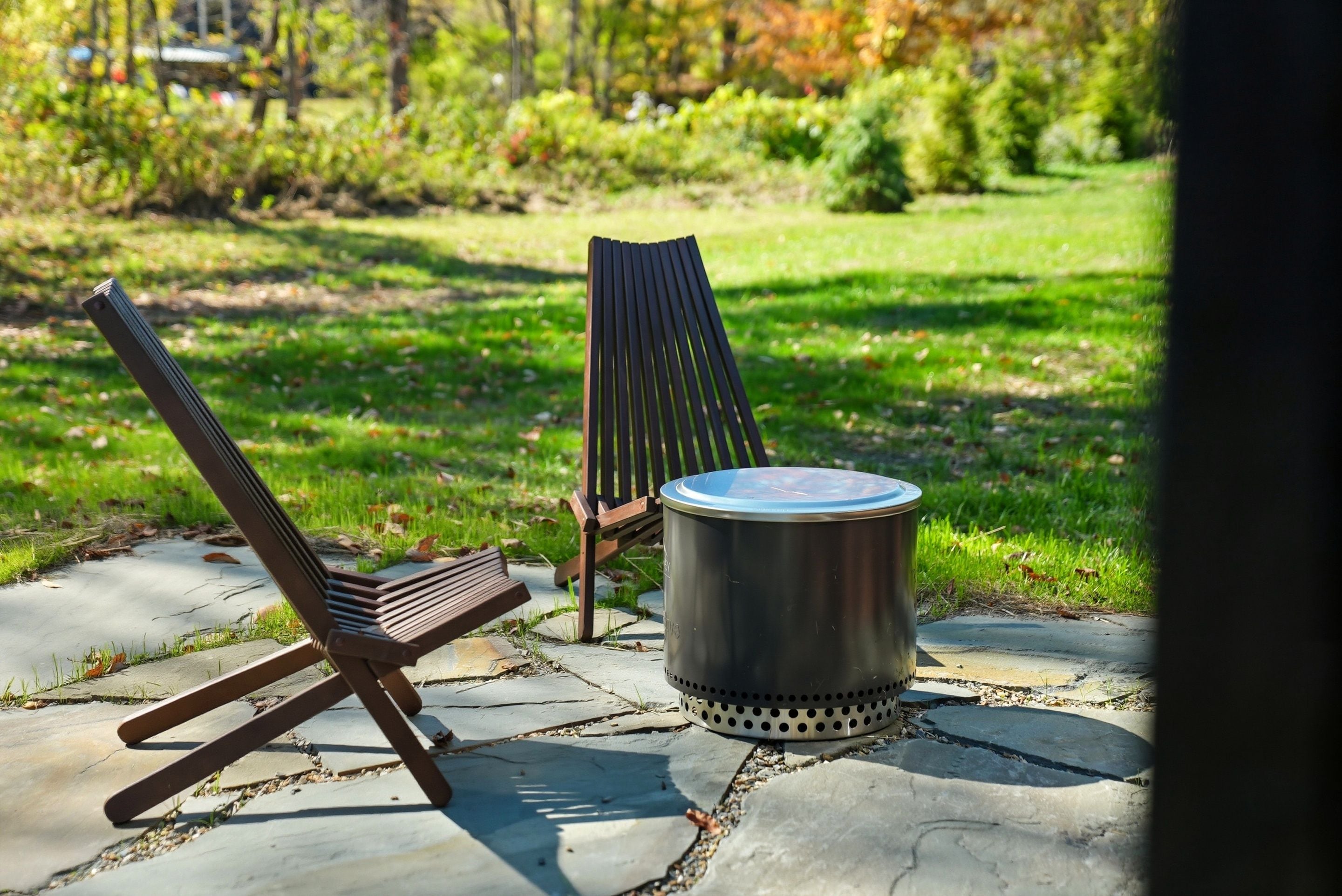 A patio with two chairs and a metal trash can.