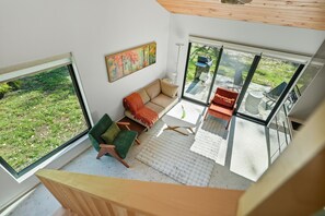 Un interior modern amb un sofà, cadires, un quadre i grans finestres que donen a l'exterior.