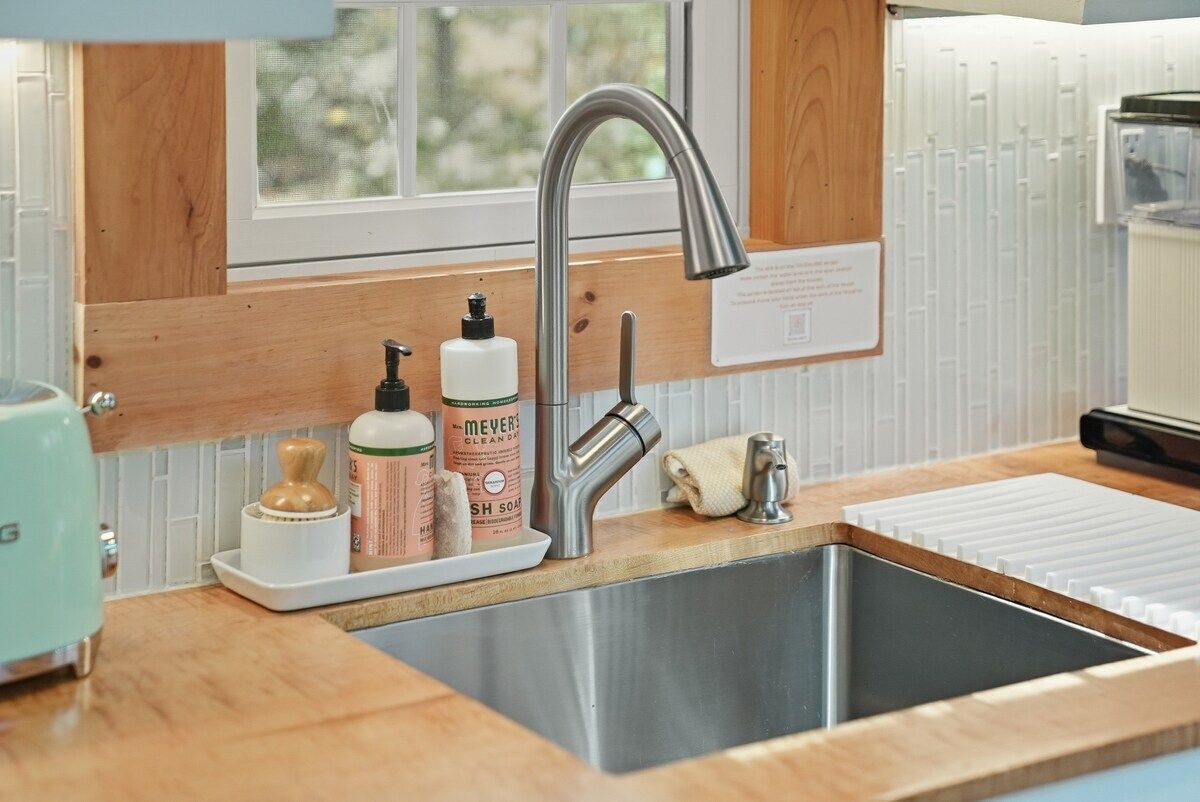 A kitchen with a stainless steel sink, wooden countertop, and a window above the sink.