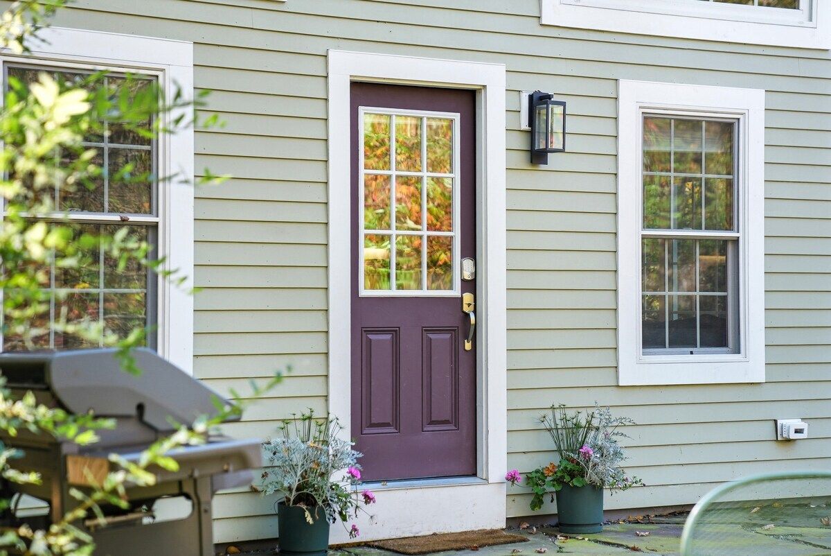 Une maison avec une porte d’entrée violette, deux fenêtres et un porche agrémenté de plantes en pot.