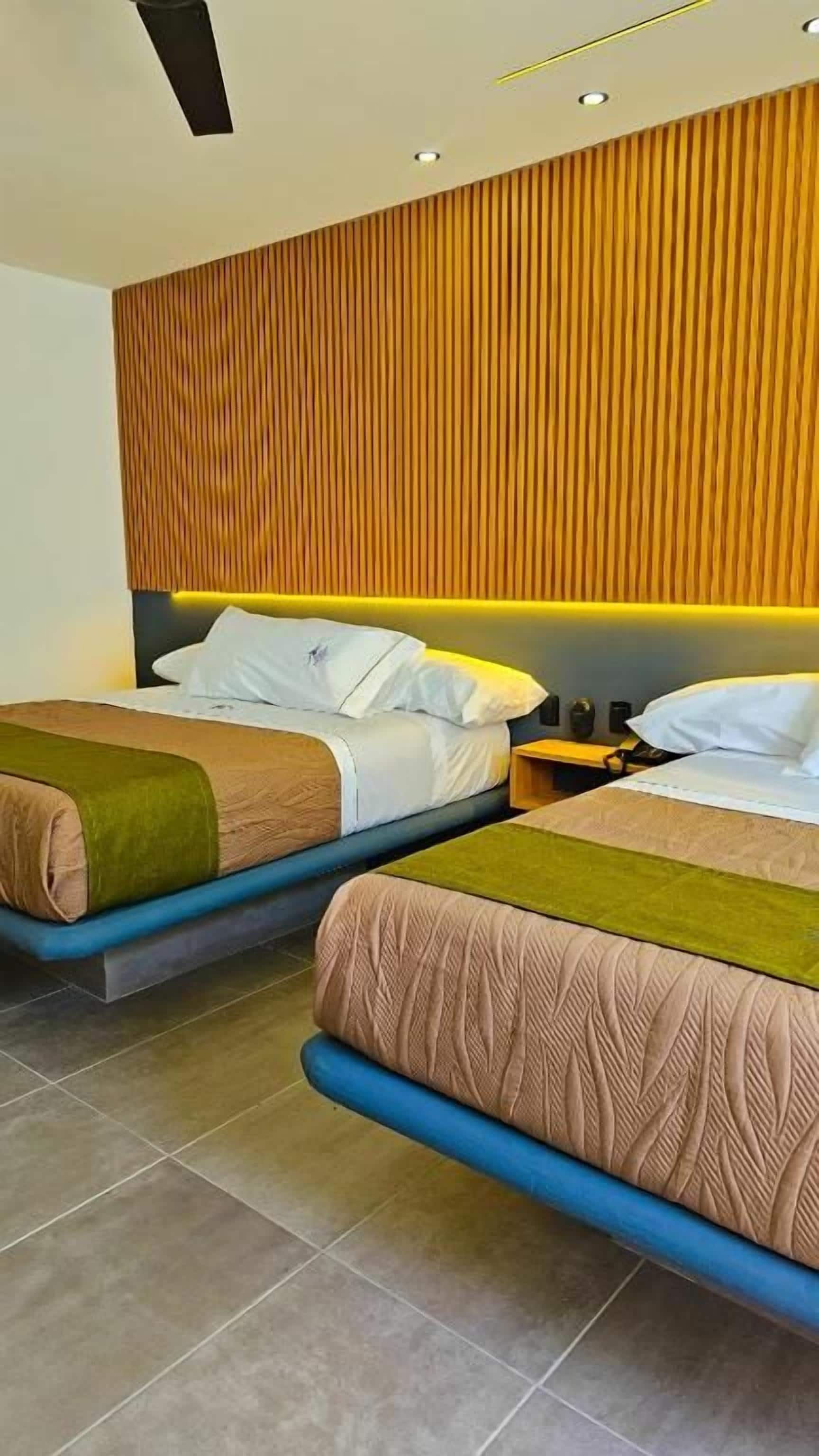 Habitación de hotel con dos camas, un cabecero de madera y una mesita de noche con una lámpara.