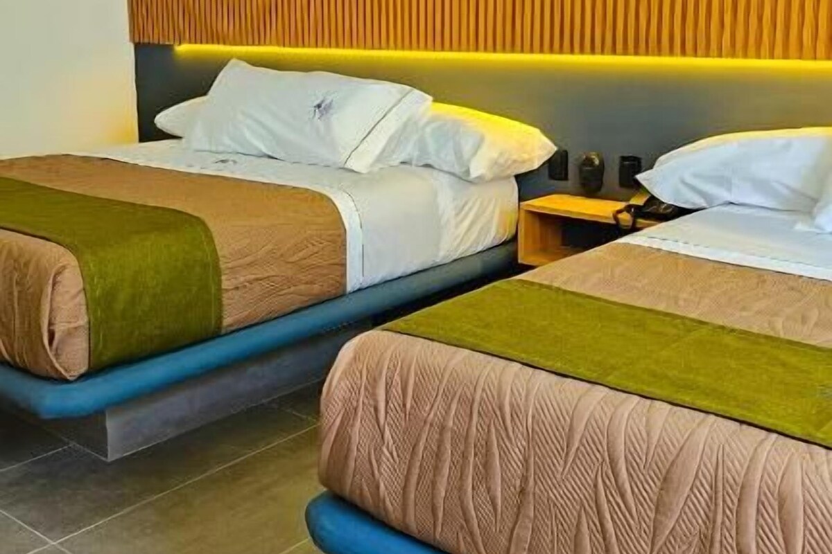 A hotel room with two beds, a wooden headboard, and a nightstand with a lamp.