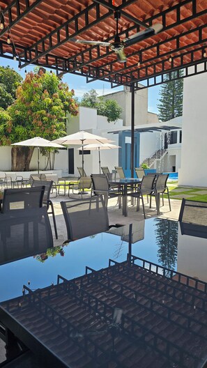 An outdoor pool area with a covered seating area, chairs, and umbrellas. - Hotel San Carlos Boutique (YAUTEPEC DE ZARAGOZA)