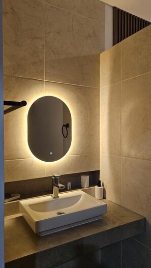 A modern bathroom with a rectangular sink, a round mirror with underglow lighting, and a dark countertop. - Hotel San Carlos Boutique (YAUTEPEC DE ZARAGOZA)