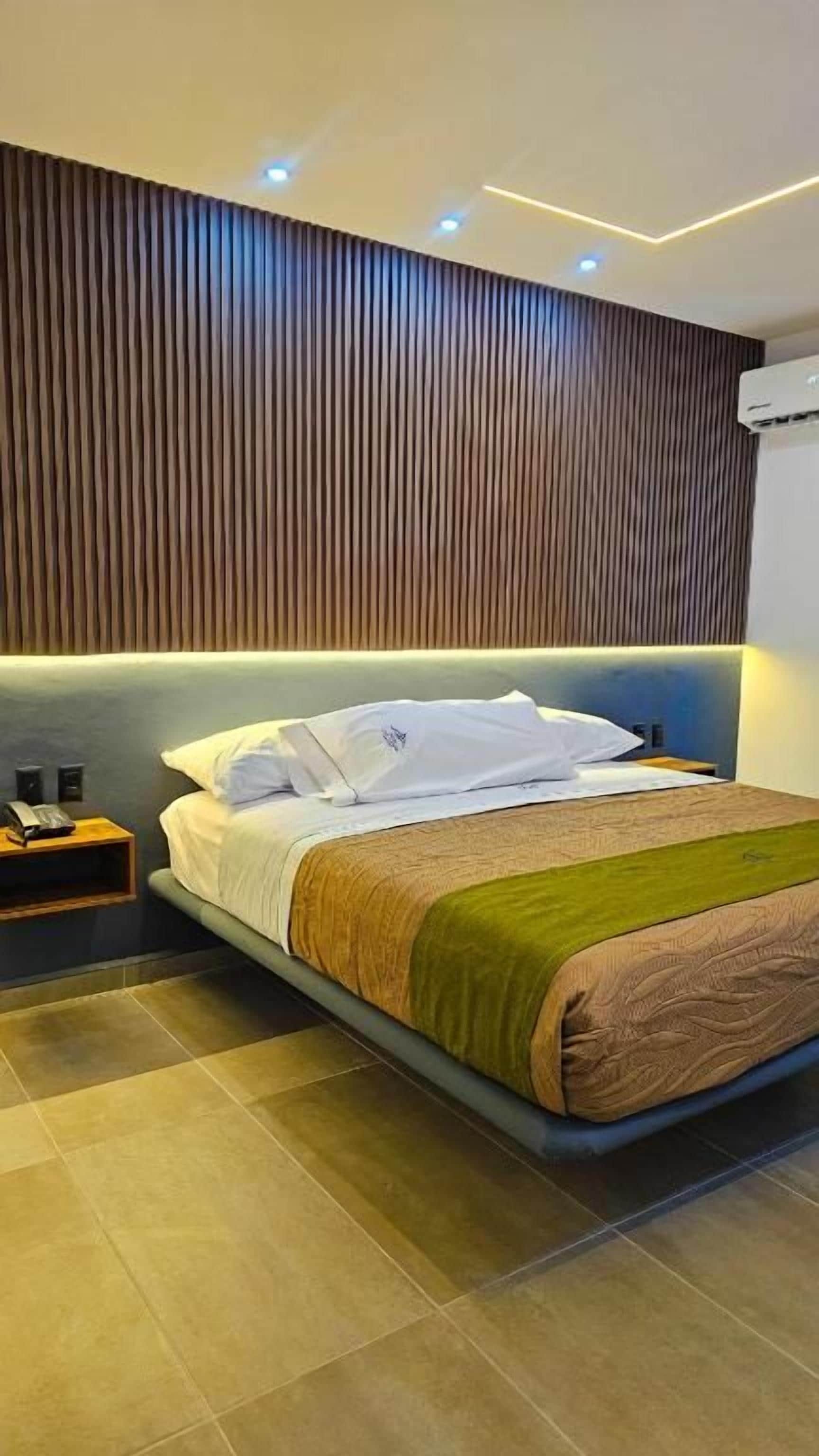 Une chambre d’hôtel moderne avec un grand lit, une tête de lit en bois et une table de chevet.