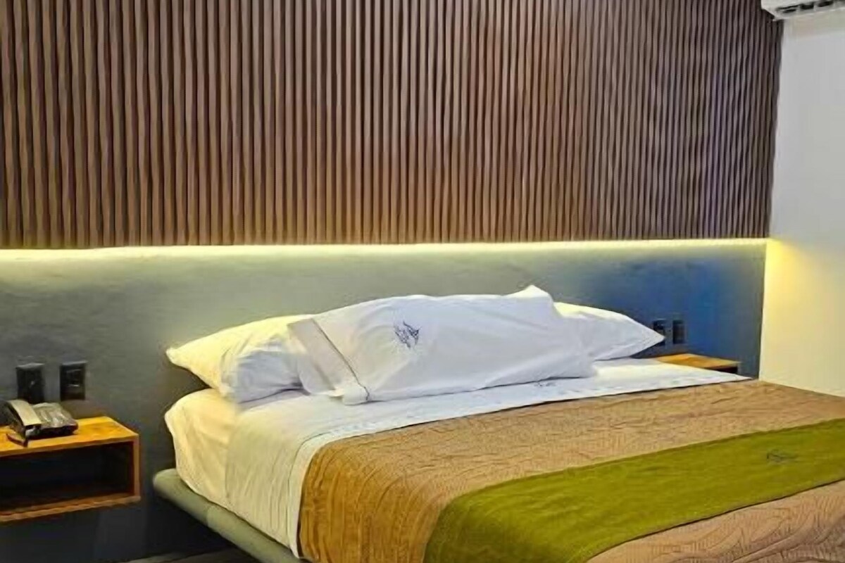 A modern hotel room with a large bed, a wooden headboard, and a nightstand.