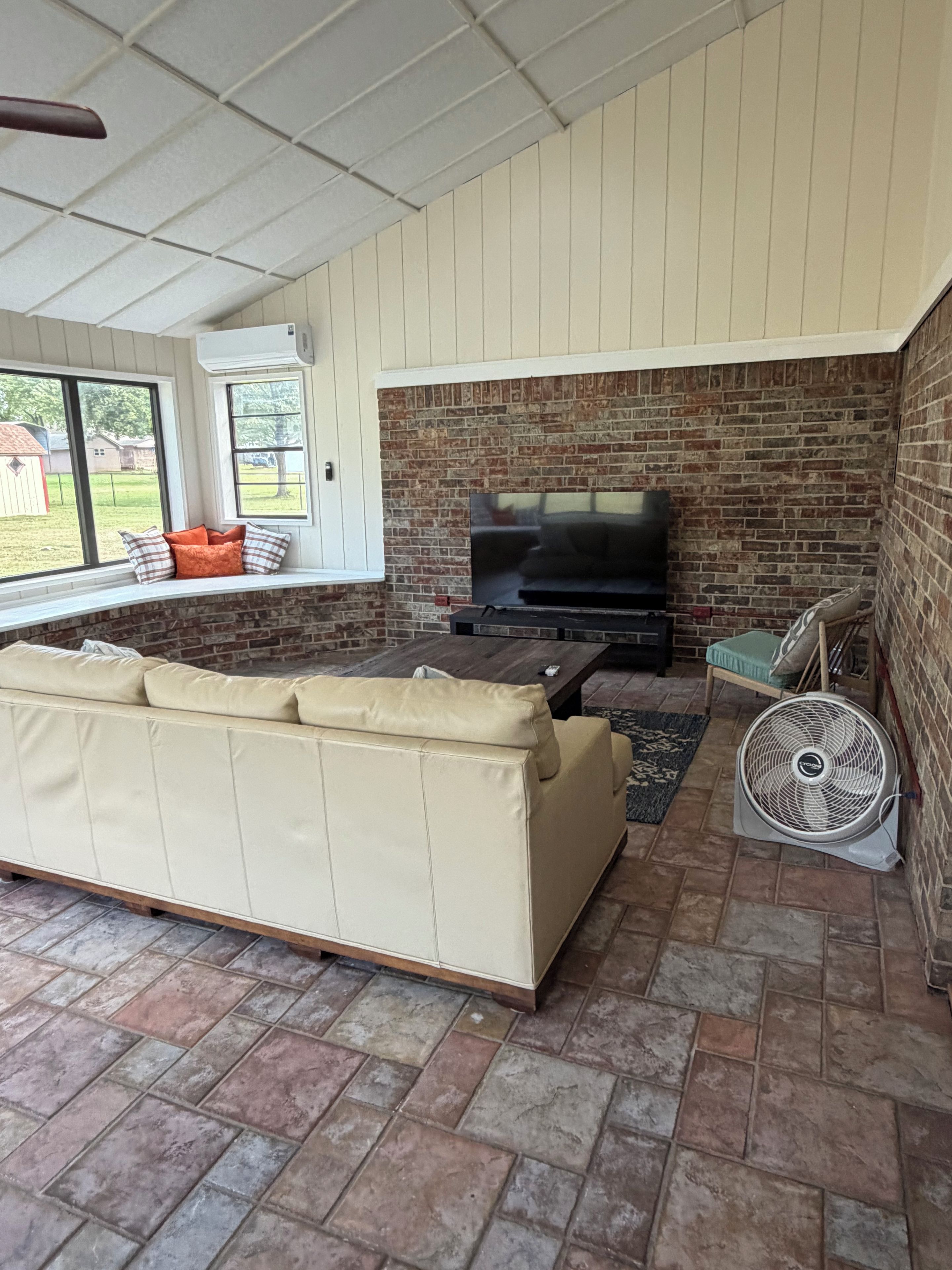 A covered outdoor seating area with a brick fireplace, a sofa, and a fan.