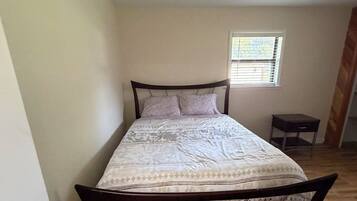 Une chambre à coucher avec un lit, un plancher en bois, une fenêtre et une petite table de chevet.