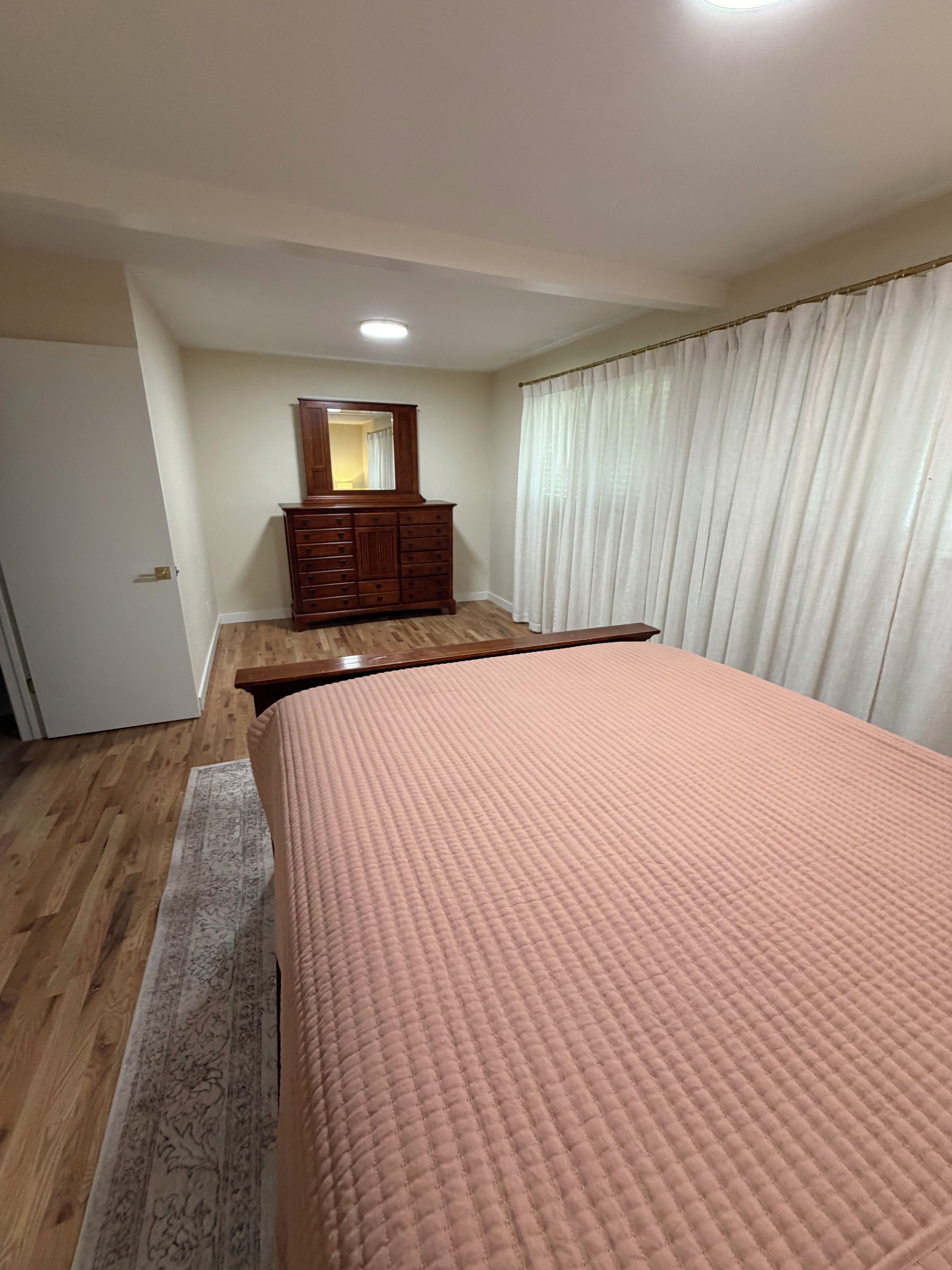 A bedroom with a bed, a dresser, a mirror, and a window with curtains.
