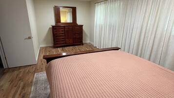 A bedroom with a bed, a dresser, a mirror, and a window with curtains.