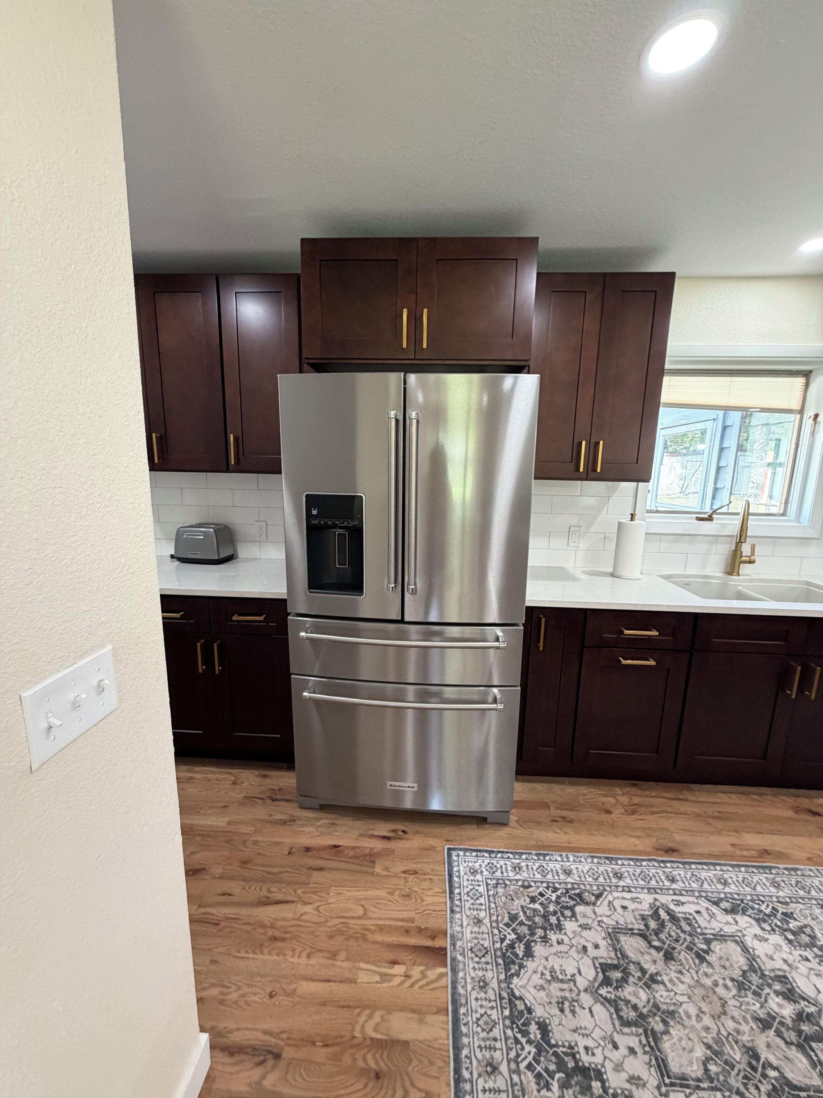 A kitchen with dark wooden cabinets, stainless steel appliances, and a patterned rug.