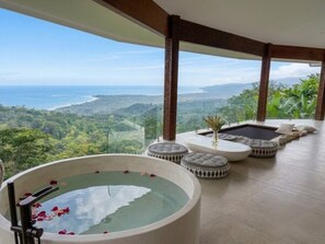 A spa area with a hot tub, seating, and a view of the ocean and hills. - Octagon Villa by Pura Villas (Bahía Ballena)