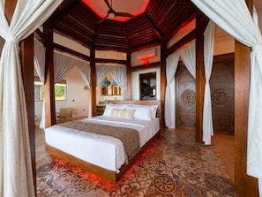A room with a large bed, wooden beams, patterned flooring, and a ceiling fan. - Octagon Villa by Pura Villas (Bahía Ballena)