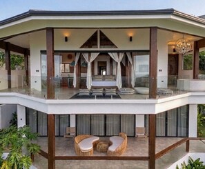 A modern multi-level house with a glass balcony, a spacious living area, and a bedroom with a large bed and curtains. - Octagon Villa by Pura Villas (Bahía Ballena)