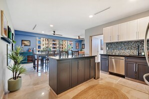 A modern kitchen with dark cabinetry, a central island, and a view of a residential building. - Medano Beach, Walk Everywhere, Pool, Jacuzzi, 2BD (Cabo San Lucas)