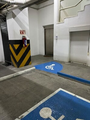 Ein Parkplatz mit einem blauen Behindertenparkplatz, einem Feuerlöscher und einer geschlossenen Aufzugtür.