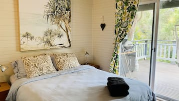 A bedroom with a large bed, patterned pillows, a heart-shaped wall decoration, and a view of a deck through a sliding glass door.