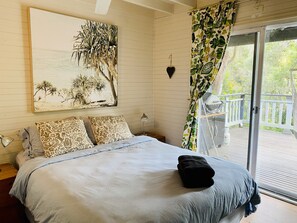 Une chambre avec un grand lit, des coussins à motifs, une décoration murale en forme de cœur et une vue sur une terrasse accessible par une porte-fenêtre coulissante.