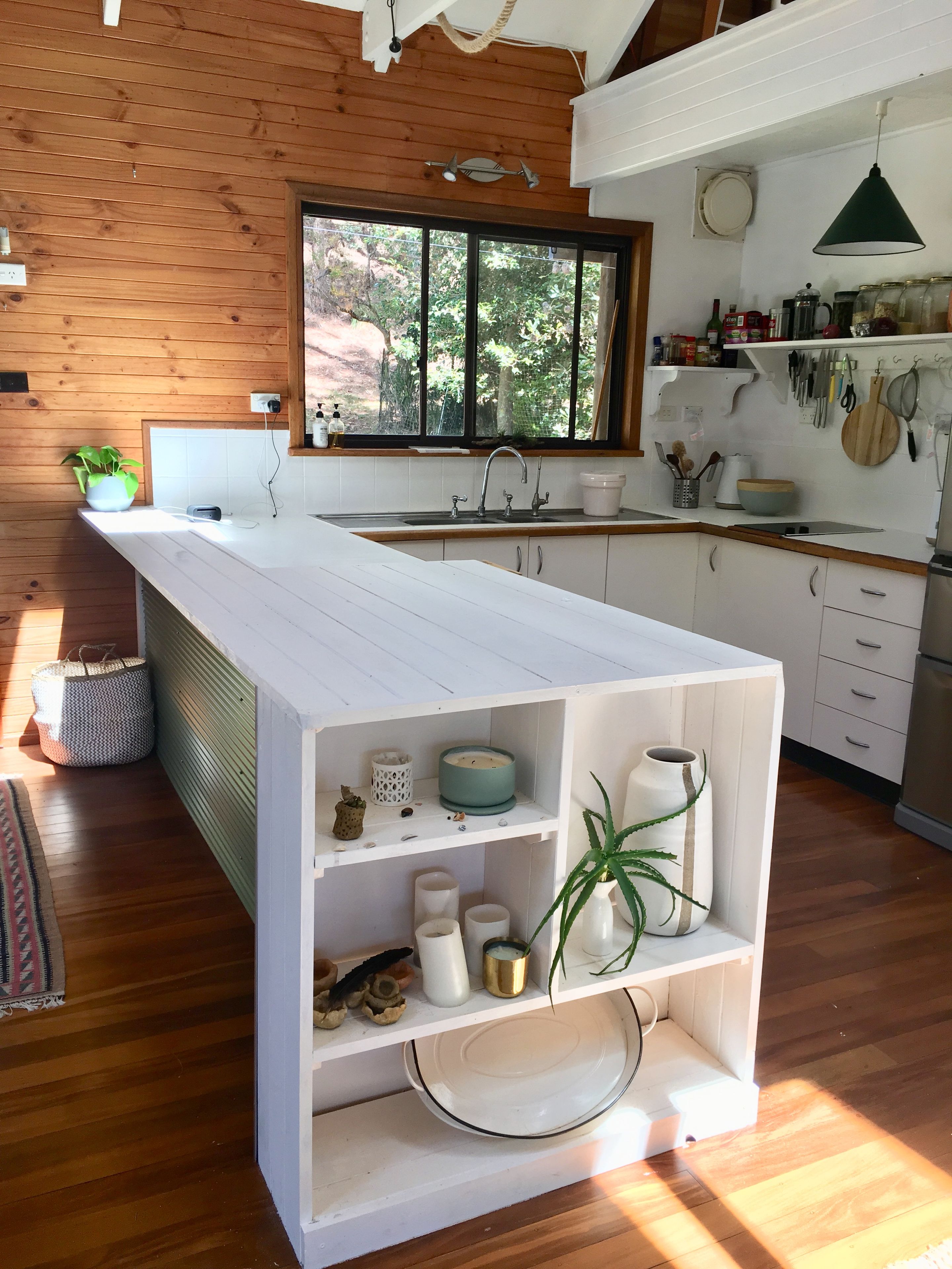A modern kitchen with a central island, wooden walls, a window with a view, and various kitchen utensils.