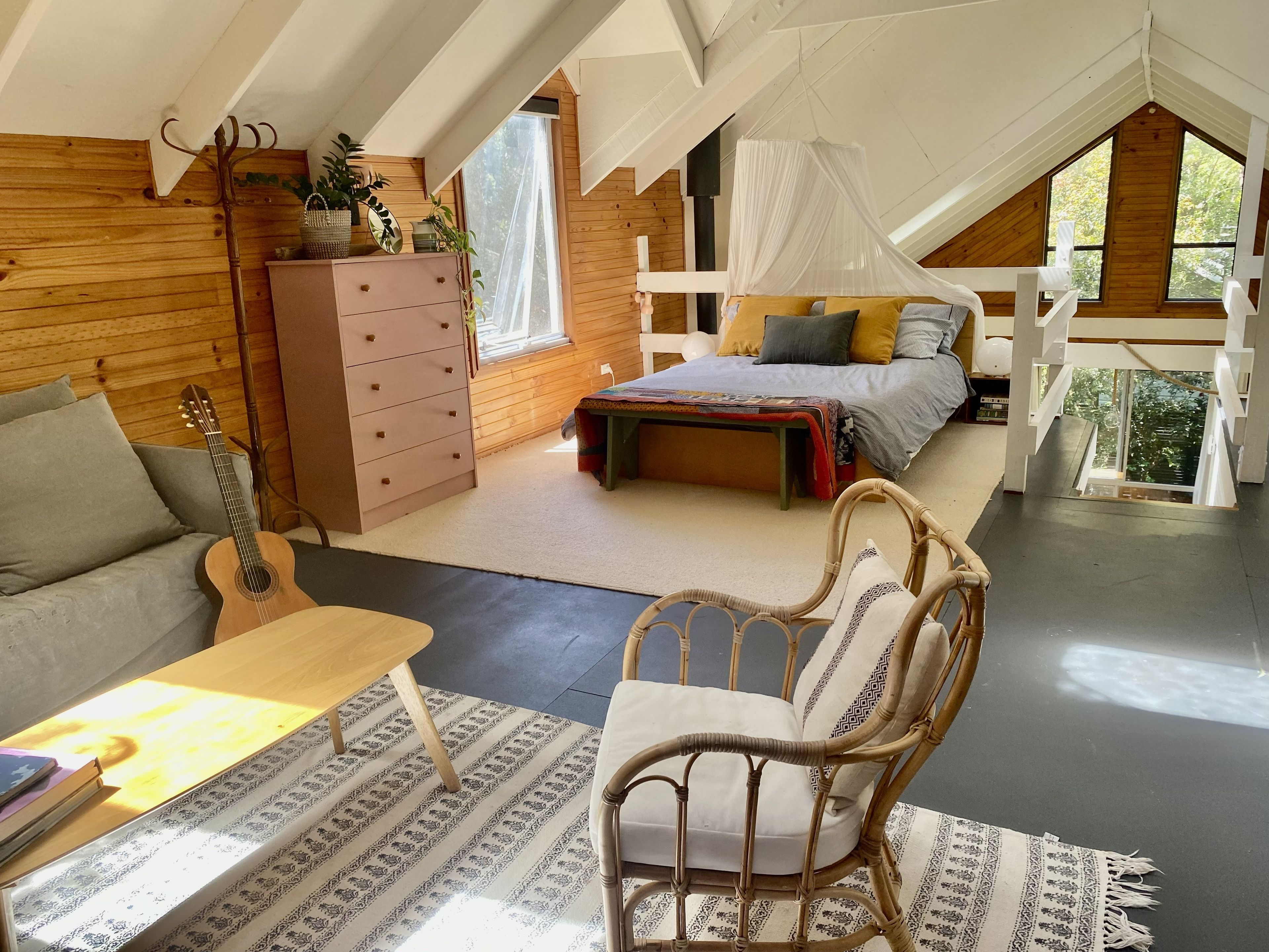 Een gezellige slaapkamer op zolder met een bed, een dressoir, een gitaar en een rieten stoel.