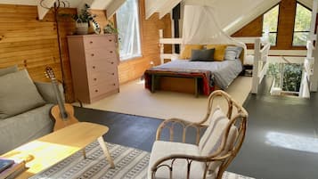 A cozy attic bedroom with a bed, a dresser, a guitar, and a wicker chair.