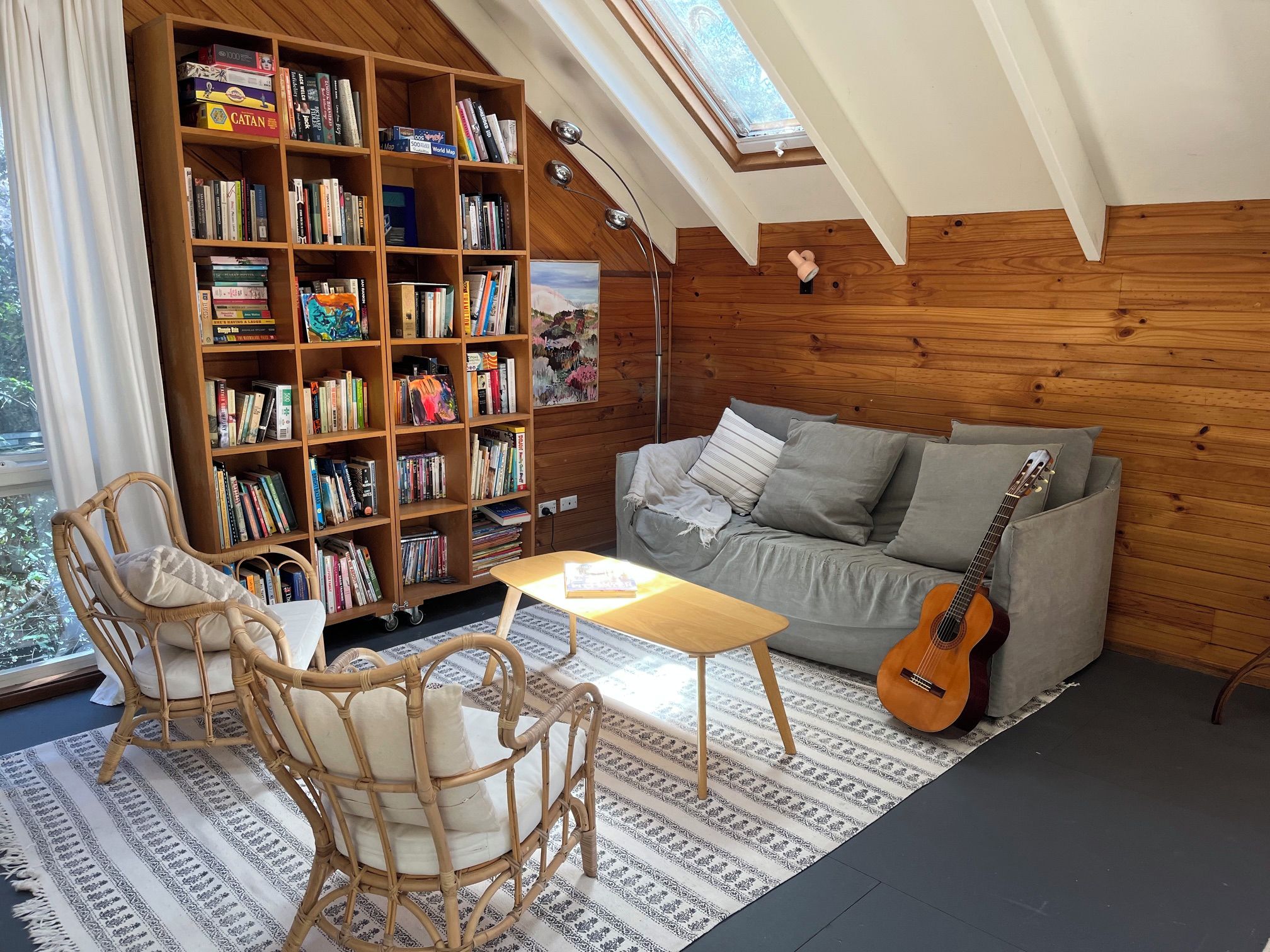 Un coin lecture confortable avec une bibliothèque, un canapé, une guitare et une table.