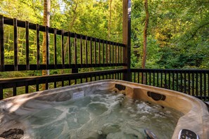 A hot tub with a warning label, surrounded by a wooden deck and a forested area. - Waterfront King Suite | Hot Tub | Forest Views | Romantic Getaway (Sevierville)