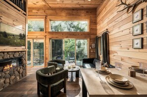 A cozy cabin interior with a stone fireplace, wooden walls, and large windows offering a view of the outdoors. - Romantic Smoky Mountain Hideaway | Waterfront (Sevierville)