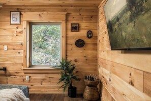 Ein Holzblockhaus-Innenraum mit Fenster, Pflanze, Schachbrett und einem gerahmten Bild an der Wand.