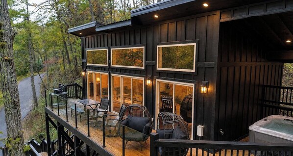 A wooden cabin with a deck, outdoor seating, and a hot tub. - Waterfront King Suite | Hot Tub | Forest Views | Romantic Getaway (Sevierville)
